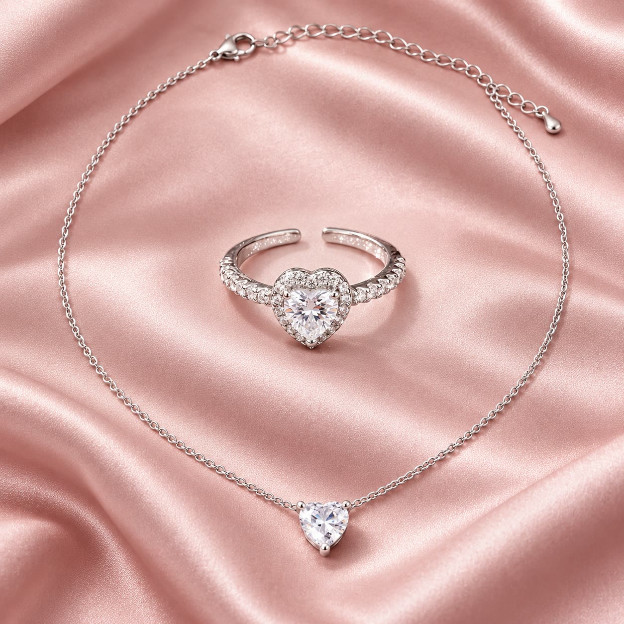 סט טבעת ושרשרת בגוון כסף עם אבנים בחיתוך לב על רקע סאטן ורוד